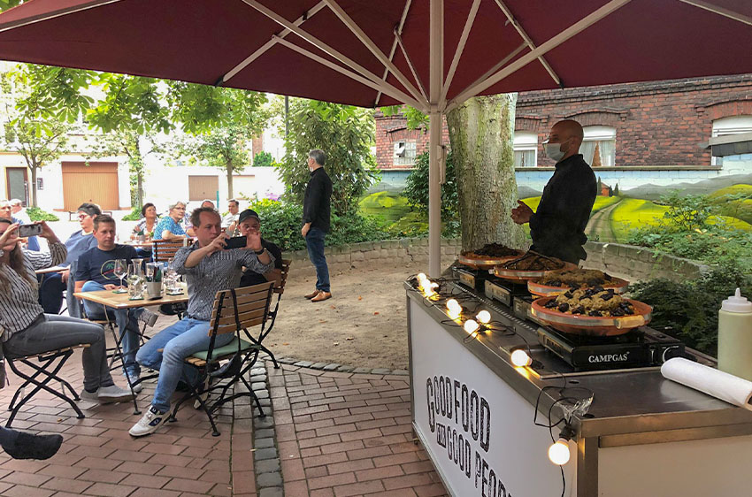Ein aufgebautes Buffet auf der Terrasse mit Gästen an Tischen