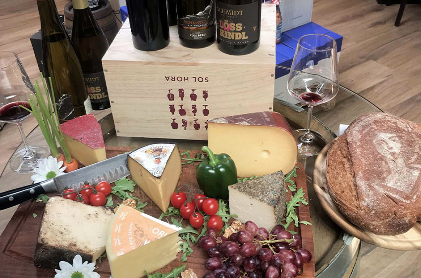 Käseplatte auf einem Tisch mit Trauben und Weinflaschen im Hintergrund