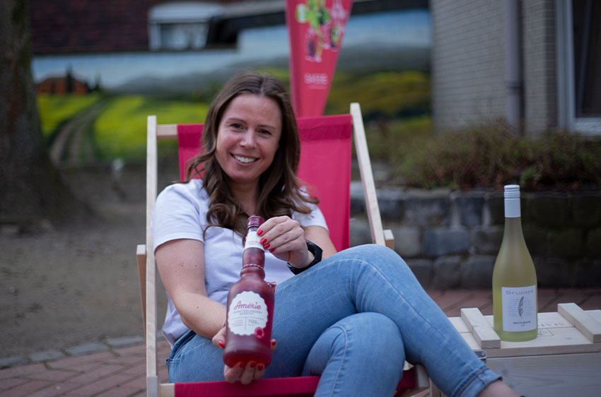 Eine lachende Frau in einer Strandliege mit Weinflasche in der Hand